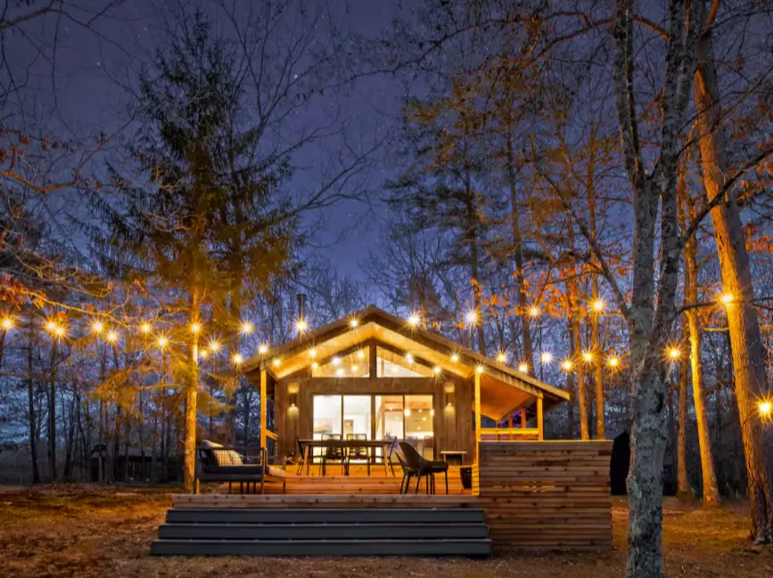 The Coalmont cabin at night under a starry Tennessee sky, with warm string lights creating an inviting glow on the modern deck.
