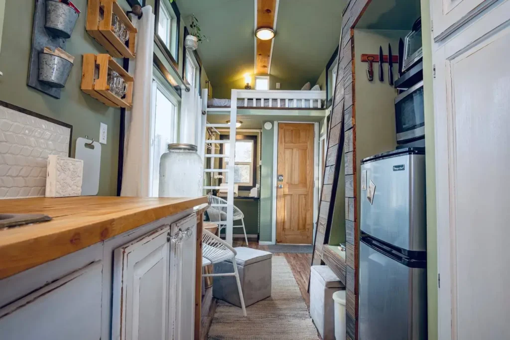 The interior layout of a 200 sq ft tiny house, showing the kitchen with a wooden countertop leading to a sleeping loft with a ladder.