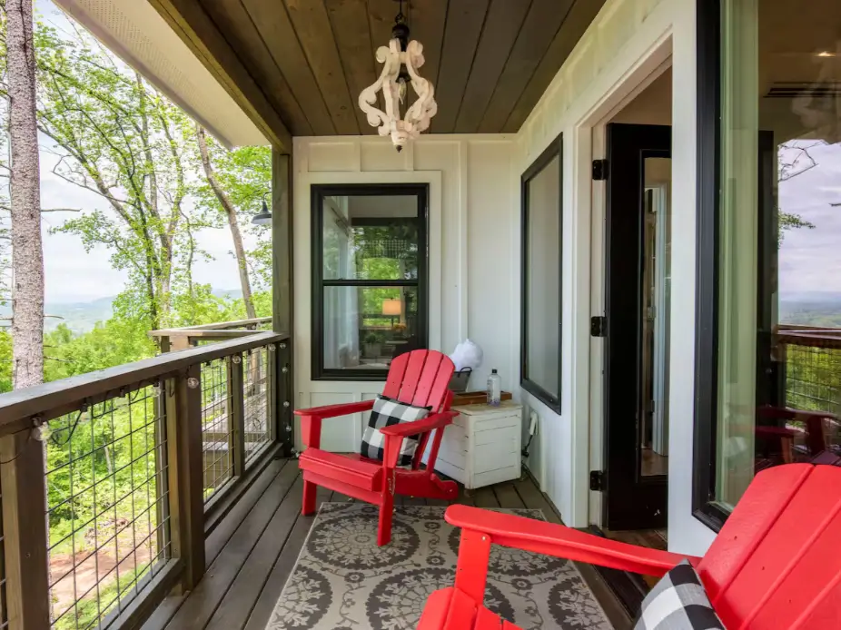 A cozy seating area on the covered porch of the Asheville farmhouse treehouse, with red chairs overlooking the mountains.