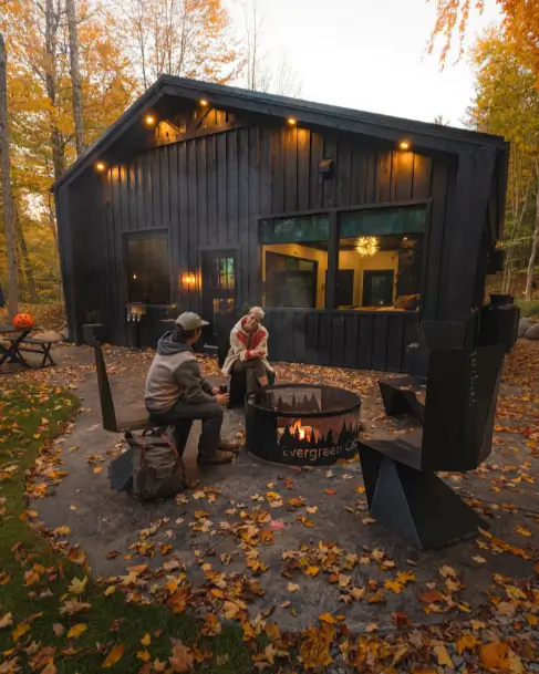 A couple enjoying a romantic evening by the fire pit on the private patio of the Birch Falls Spa Cabin during autumn.