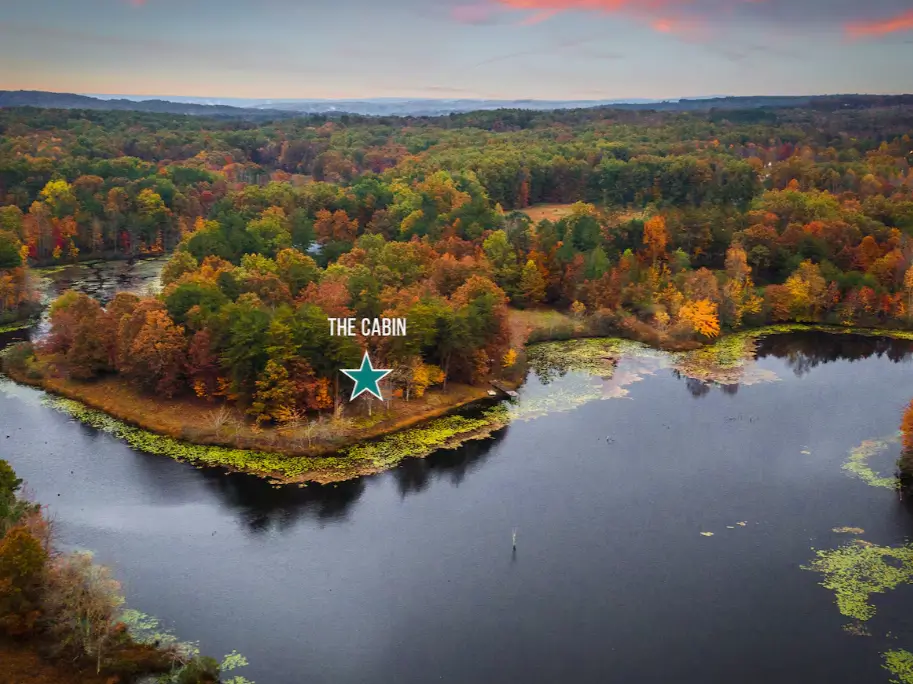An aerial view of The Coalmont cabin nestled on a peninsula surrounded by a private lake and dense, colorful autumn foliage in Tennessee.