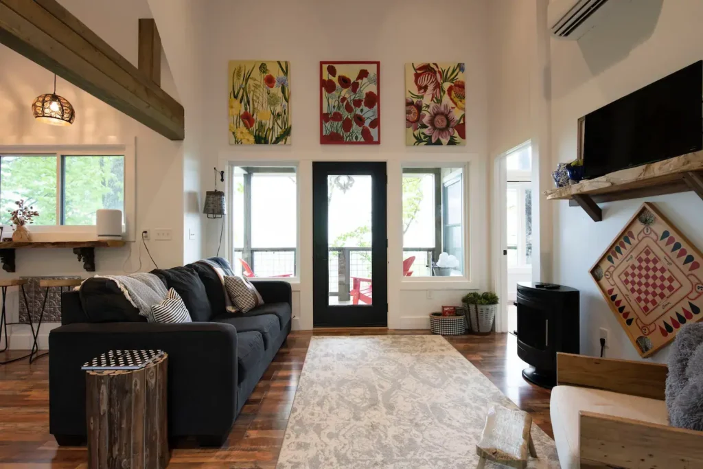The inviting living room of the modern farmhouse treehouse in Asheville, featuring a comfortable sofa, rustic wood accents, and vibrant floral art.