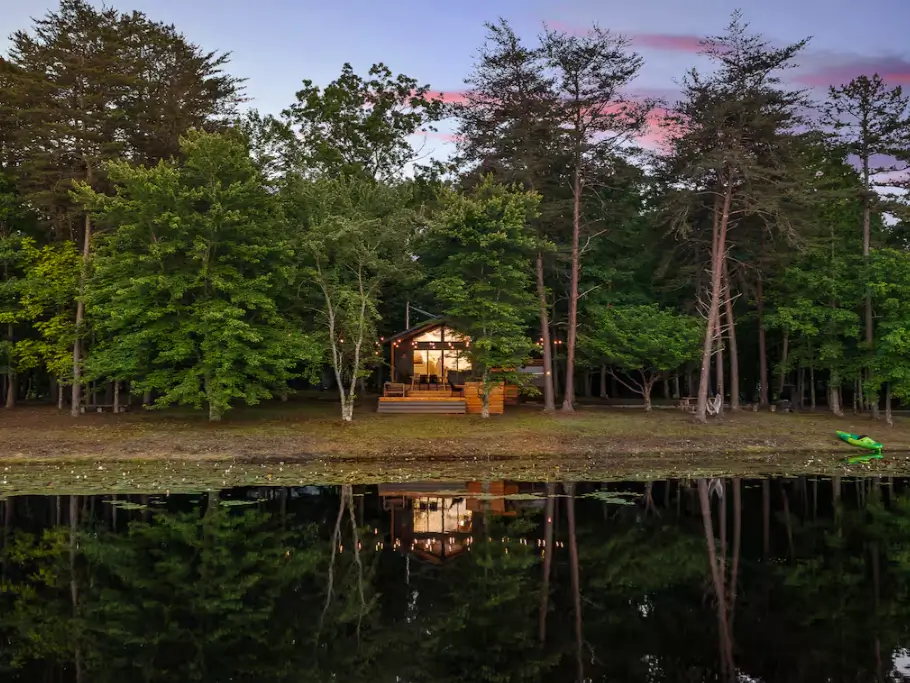 The Coalmont cabin reflected in the calm lake at sunset, with a green kayak resting on the shore, highlighting the property's waterfront amenities.