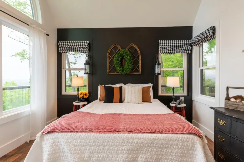 The cozy queen bedroom in the Asheville farmhouse treehouse, with a striking dark accent wall and windows offering serene mountain views.