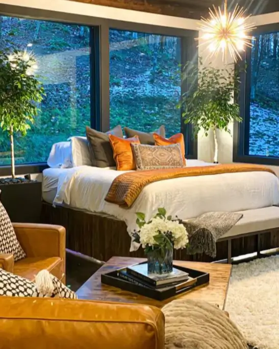 The plush king-sized bed in the Birch Falls Spa Cabin, positioned in front of large windows with a view of the surrounding forest.