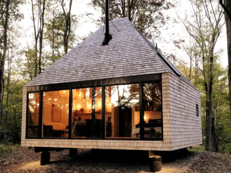 A modern 600 sq ft tiny house with cedar shake siding and large windows, nestled in a tranquil forest setting.