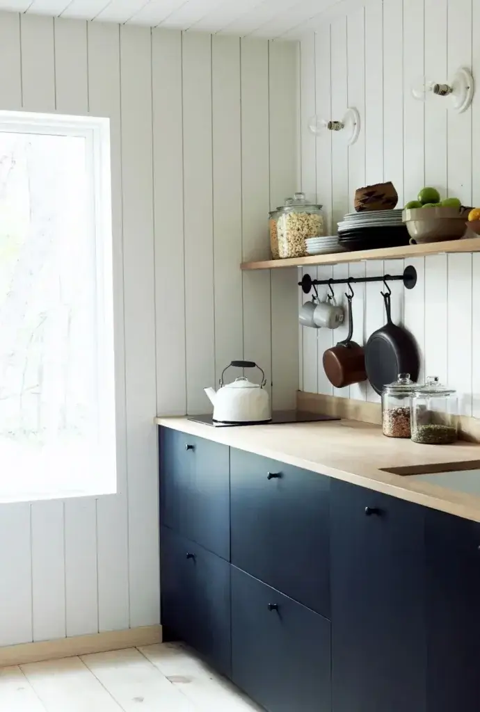 A functional and stylish tiny house kitchen with dark blue cabinets, wood countertops, and smart storage solutions like open shelving.