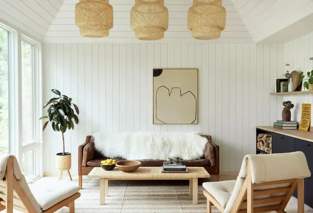 The bright and airy living room of a 600 sq ft tiny house, featuring a light color palette, leather sofa, and vertical shiplap walls to create a sense of space.