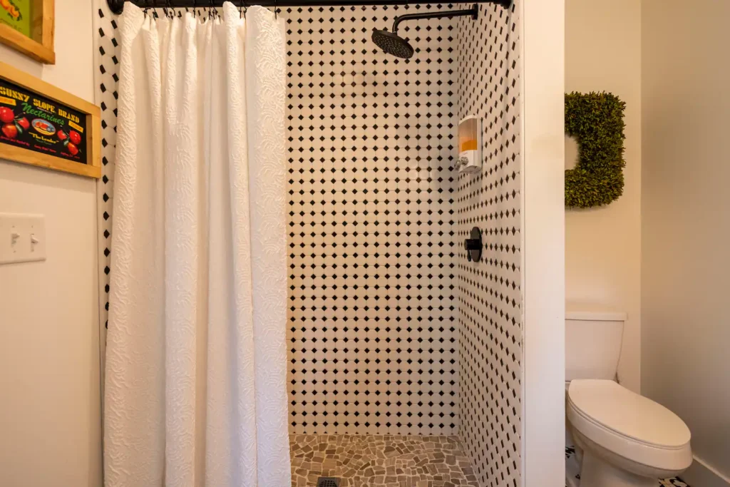 The stylish bathroom in the Asheville treehouse, featuring classic black and white patterned tile, a modern rain shower head, and a pebble stone shower floor.