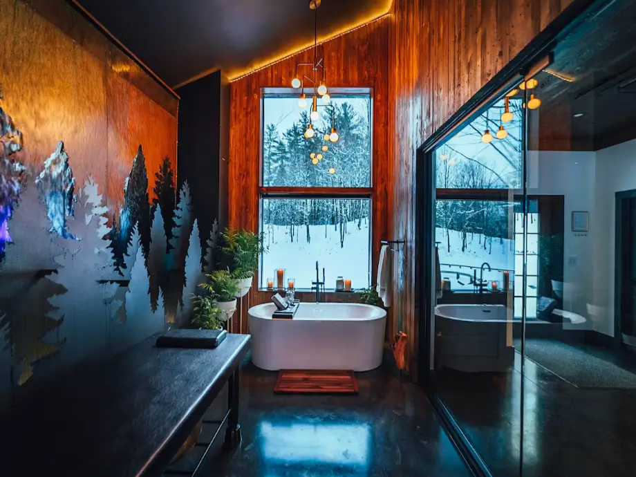 The luxurious private spa room at Birch Falls Spa Cabin, featuring a soaker tub, massage table, and a large window with a snowy winter view.
