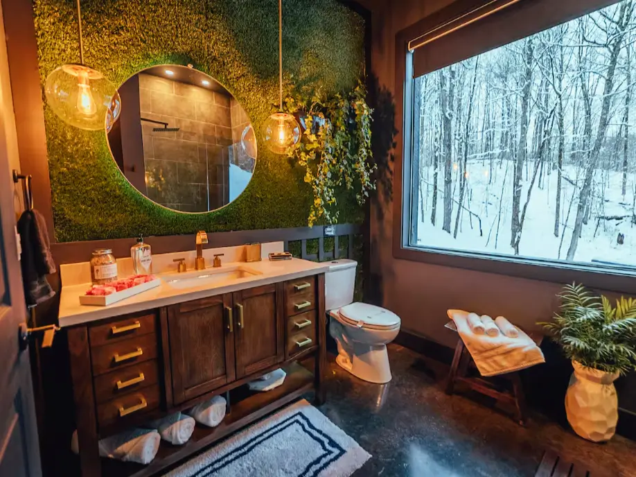 The unique bathroom at Birch Falls Spa Cabin with a biophilic moss wall, modern vanity, and a window looking out into the snowy woods.