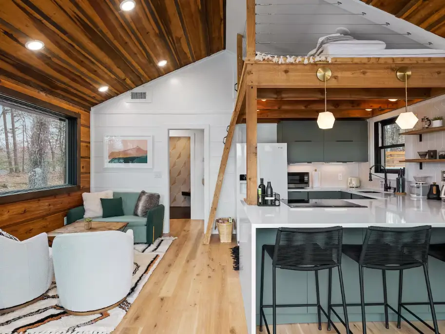 The open-concept interior of The Coalmont cabin, showing the kitchen with bar seating, the living room area, and the cozy sleeping loft above.