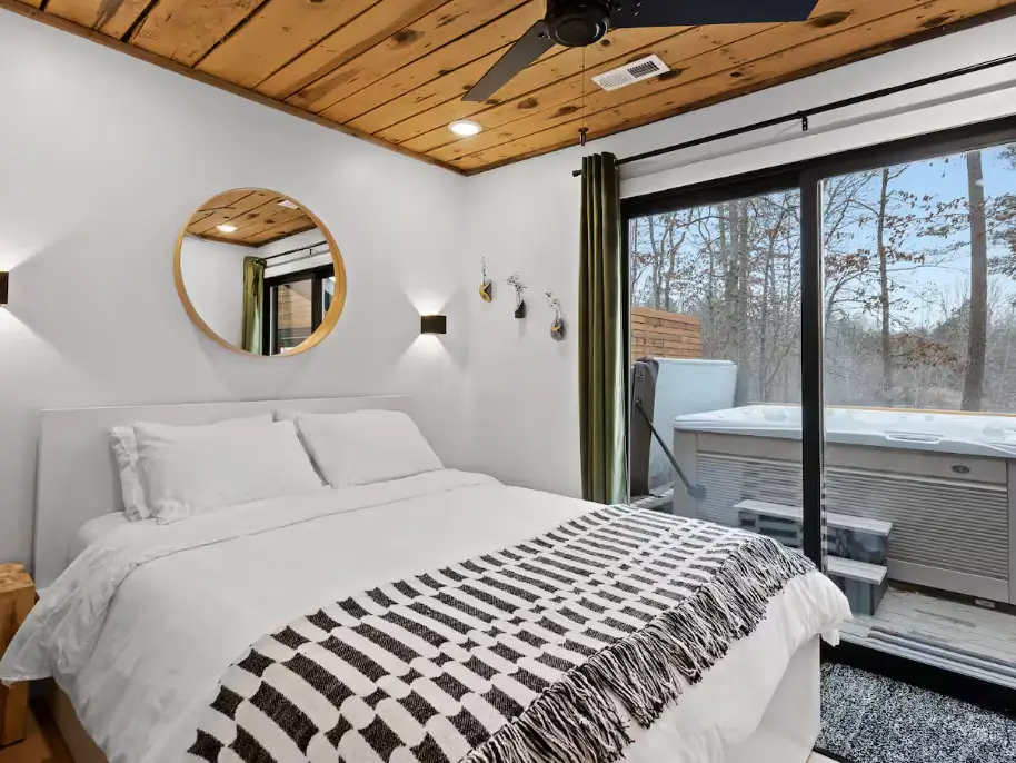 The modern bedroom at The Coalmont cabin, featuring a queen bed, wood-paneled ceiling, and a sliding glass door opening directly to the private hot tub.