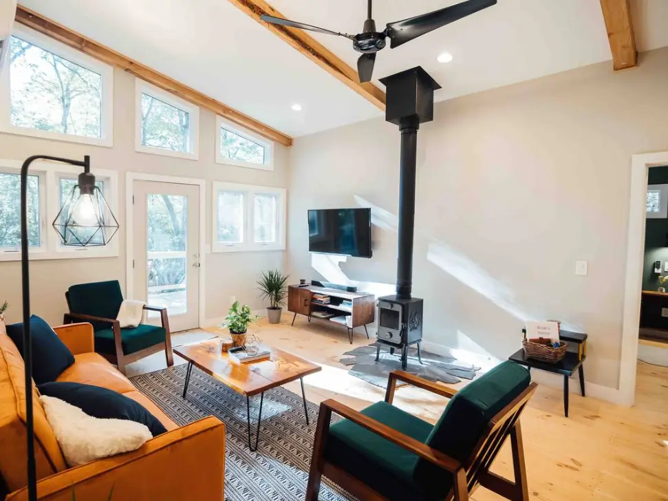 The modern and airy living room of the Trahlyta cabin, featuring a wood-burning stove and vaulted ceilings.