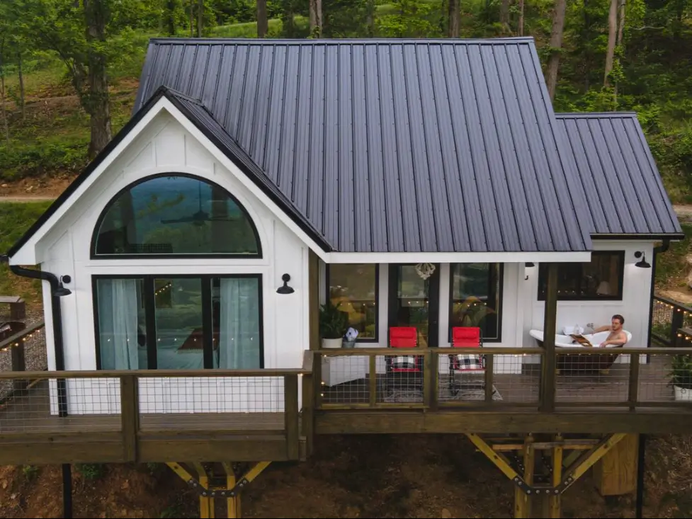 A guest relaxing in the outdoor soaking tub on the deck of the modern farmhouse treehouse in Asheville, enjoying the mountain views.