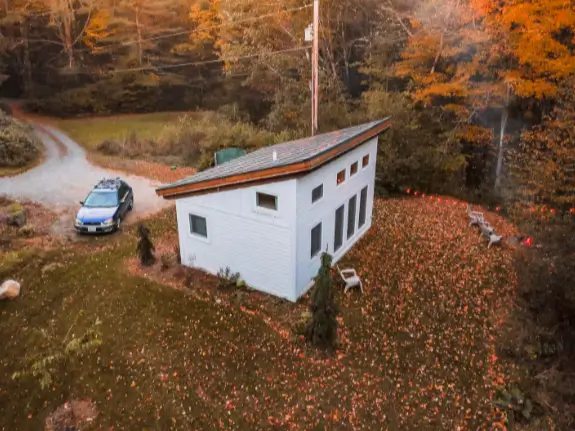 An aerial view of the Honeycrisp Cottage, a 2-bedroom tiny house, nestled in the Vermont woods during autumn.