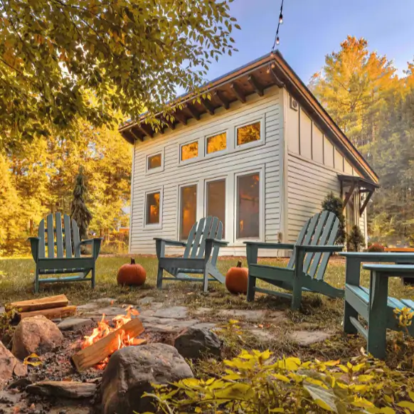 The exterior of the Honeycrisp Cottage in the fall, with a crackling fire pit and Adirondack chairs creating an inviting outdoor living space.