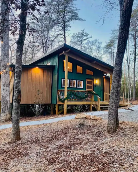 The exterior of the modern 900 sq ft Trahlyta cabin nestled in a wooded setting at dusk, with warm lights glowing from inside.