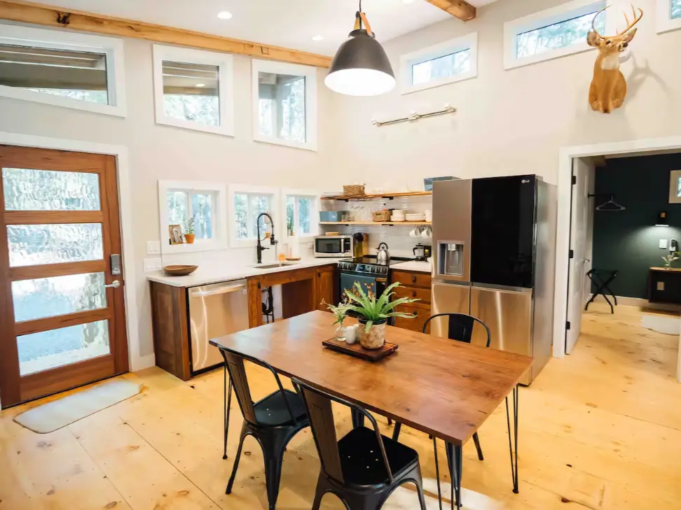 The open-concept kitchen and dining area in the 900 sq ft cabin with modern appliances and a wooden dining table.