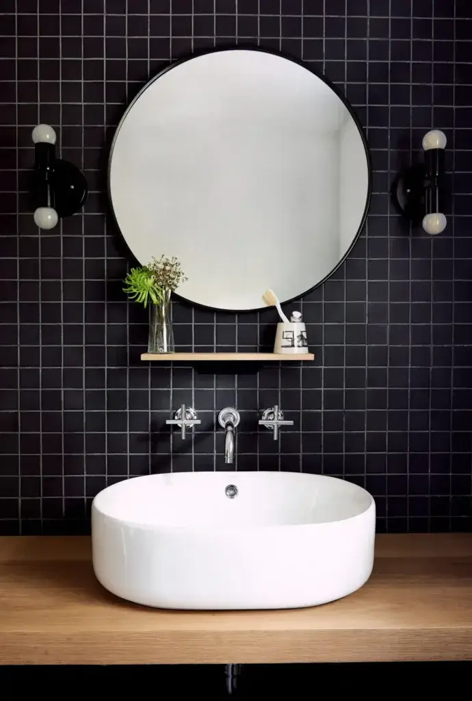 A modern tiny house bathroom with bold black square tiles, a round mirror, and a vessel sink, showcasing high-end design.