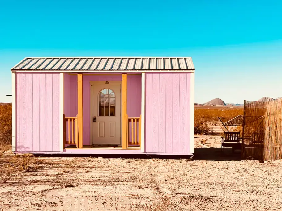 The front entrance of a charming one-bedroom tiny house, featuring a small covered porch and pink siding, showcasing a practical small house design.