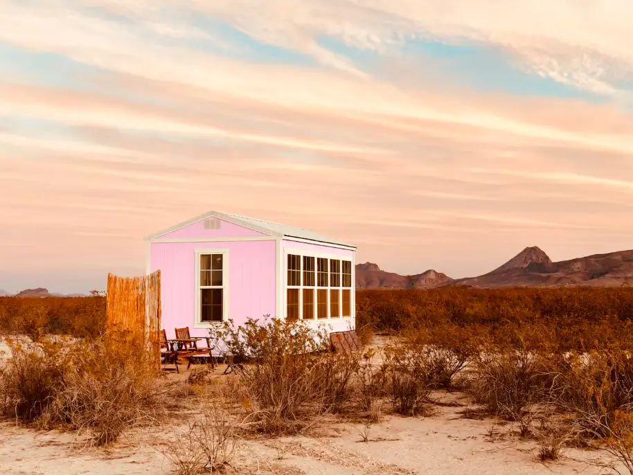 A unique one-bedroom tiny house painted pink, set in a vast desert landscape at sunset, showcasing creative small house design ideas.