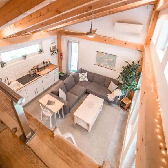 A view from the loft of the Honeycrisp Cottage, showcasing the open floor plan, vaulted ceiling with exposed beams, and the cozy 2 bedroom tiny house interior.