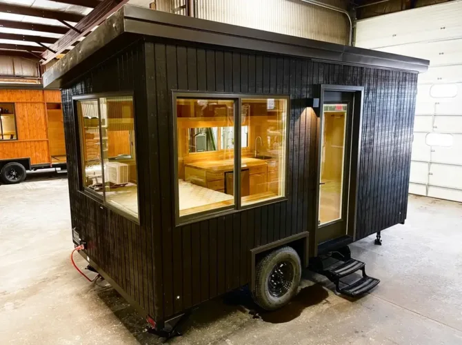 The all-black eBoho GO, a modern tiny home on wheels, a versatile prefab home for under 50k shown in a workshop.