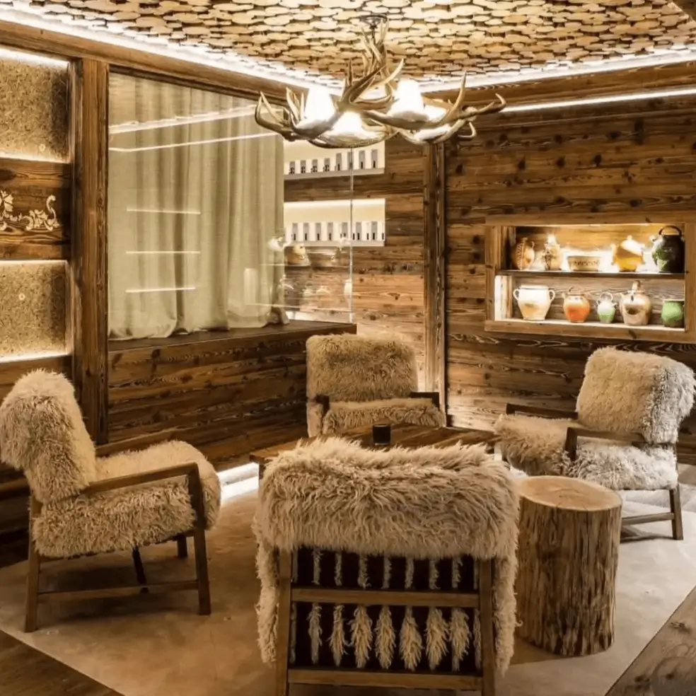 Modern rustic sitting room with a log-slice ceiling, antler chandelier, and sheepskin-covered chairs.