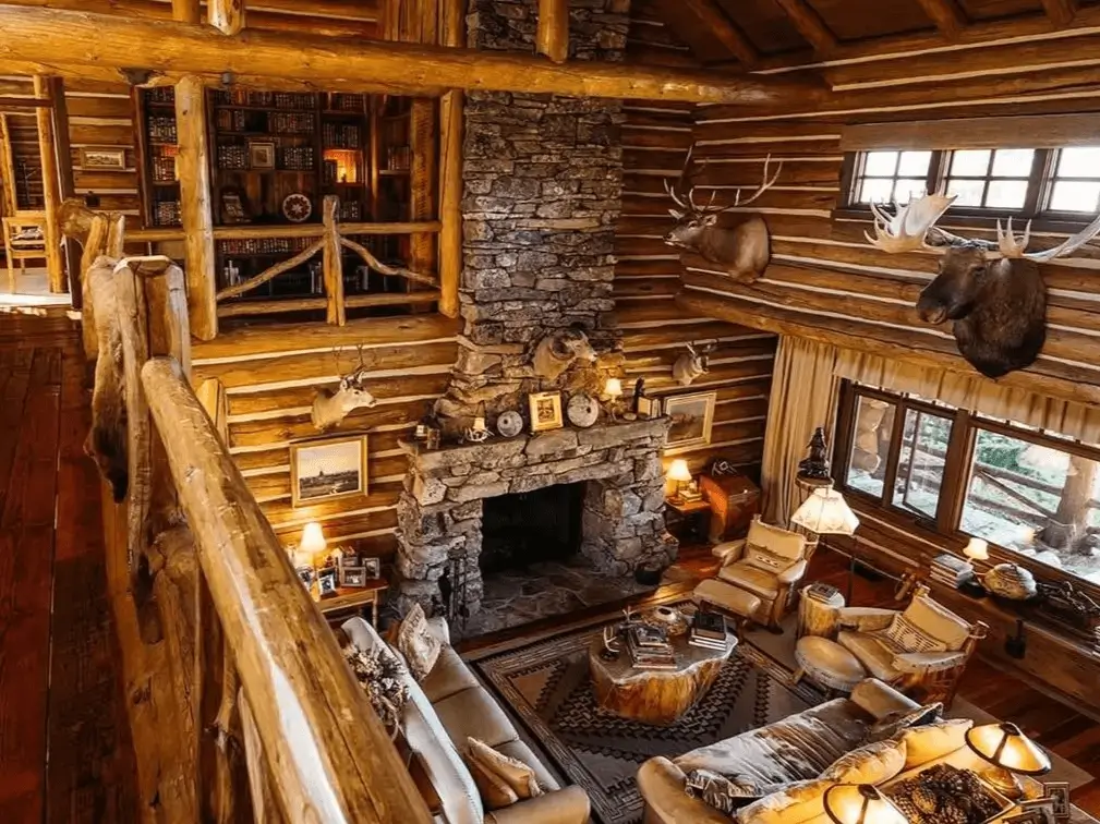 View from a loft overlooking a two-story log cabin great room with a massive stone fireplace.