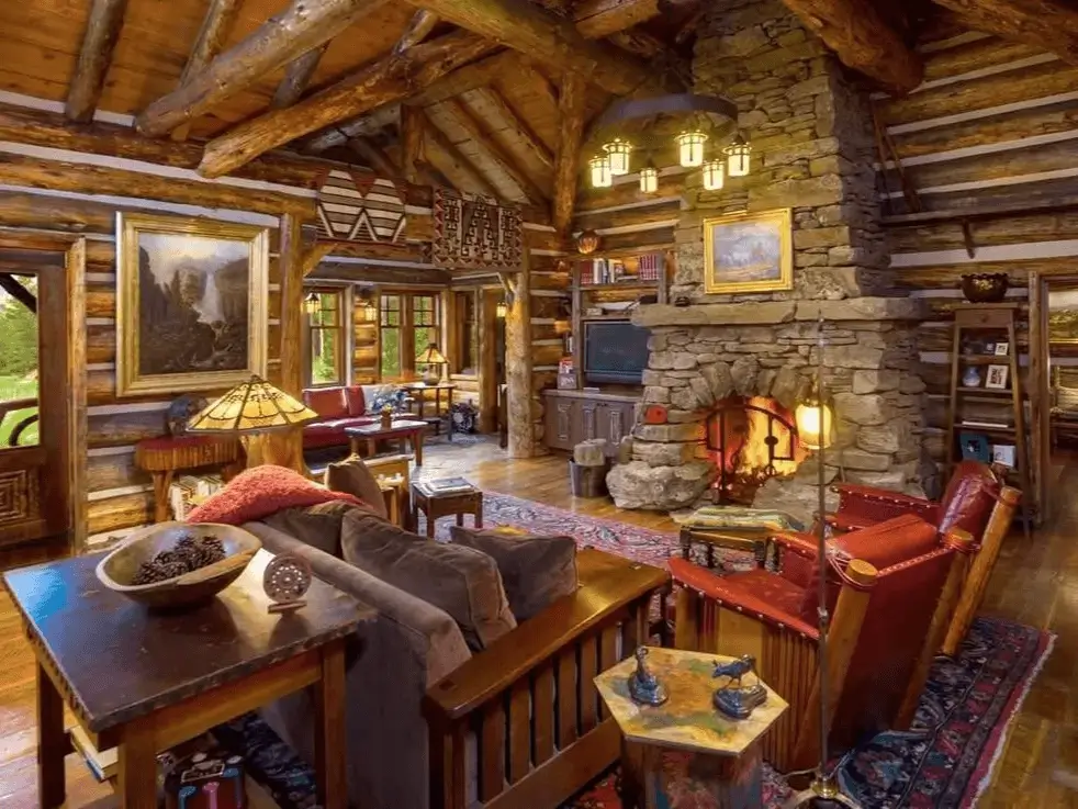 Rustic log cabin living room with multiple seating areas arranged around a central stone fireplace.