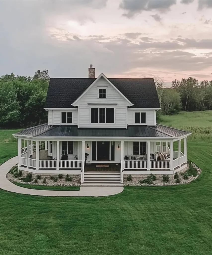 Modern farmhouse with white siding, a black roof, dormers, a side-entry garage, and surrounded by fall foliage.