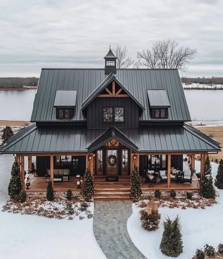 Farmhouse with a long, tree-lined driveway, wooden fencing, a stone facade, dormers, and a metal roof.