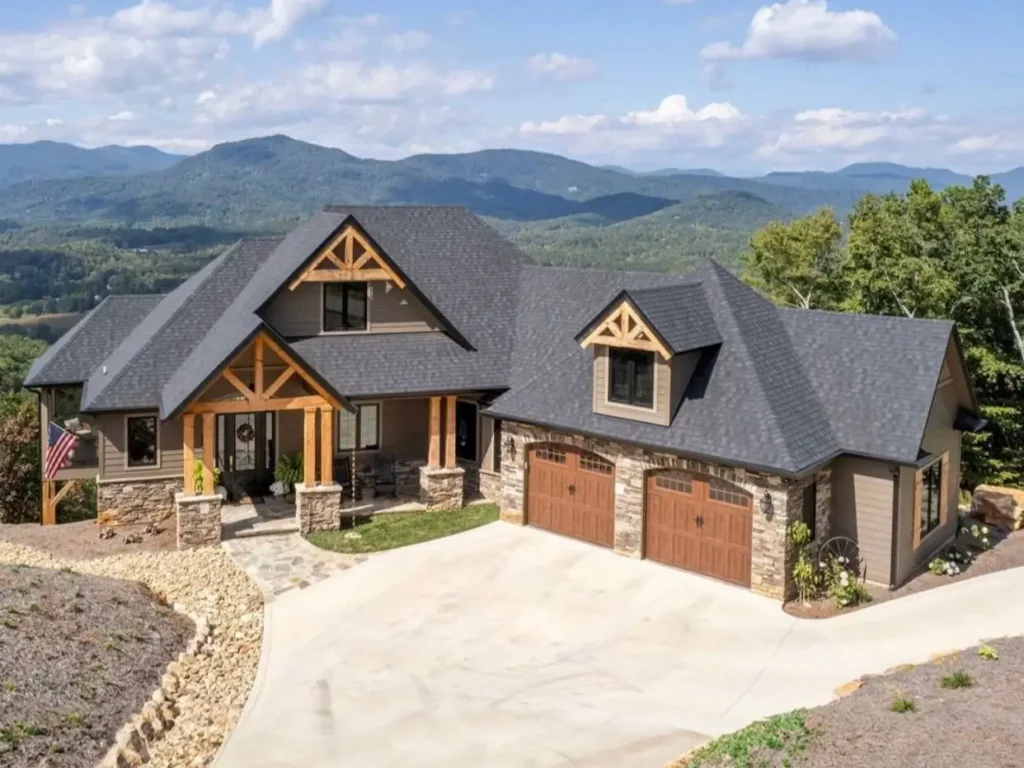 A craftsman-style luxury mountain home with timber-frame details and sweeping mountain range views in the background.