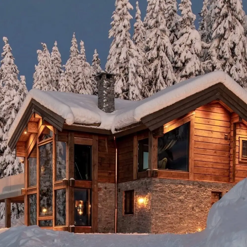 A cozy log and stone mountain cabin covered in snow, with glowing windows at dusk.