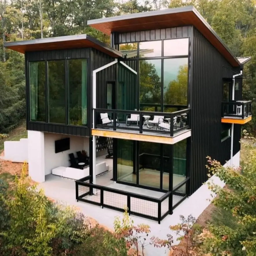 A modern, multi-level mountain home with black siding, large windows, and stacked balconies in a forest setting.