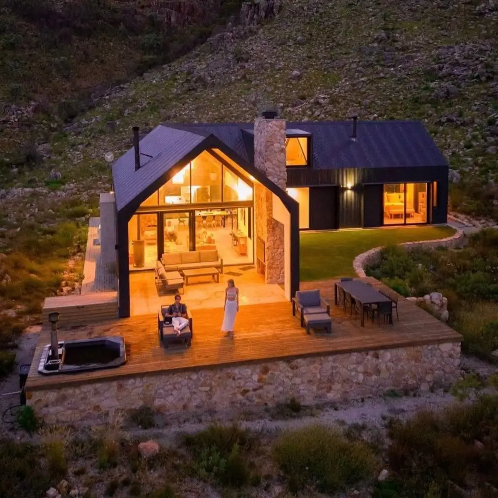 An aerial view of a modern mountain home's expansive deck with a hot tub and dining area at dusk.