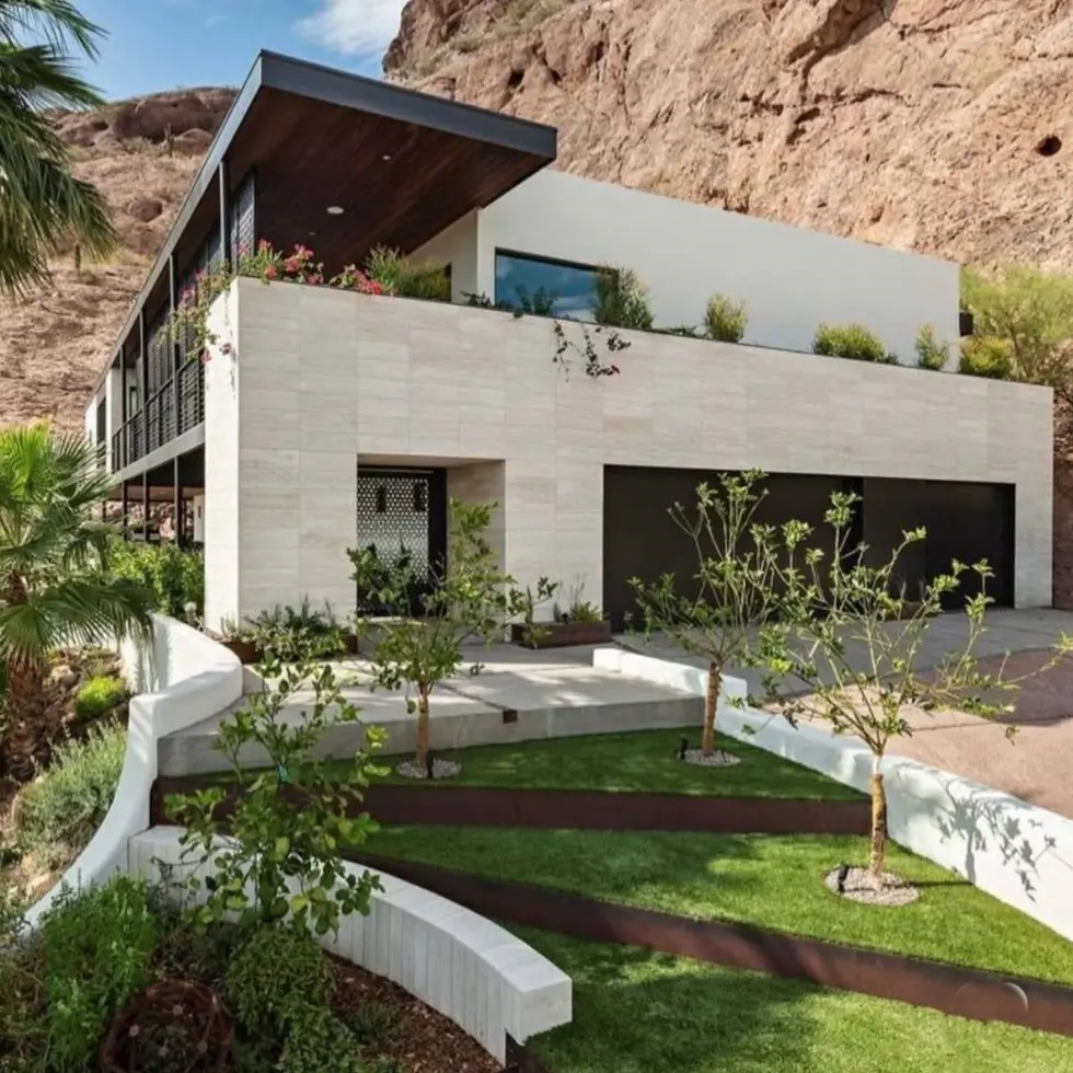 A modern desert mountain home with a white exterior built directly into a red rock cliffside.