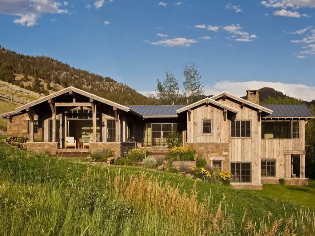 A modern rustic mountain home with weathered wood siding nestled into a grassy hillside.