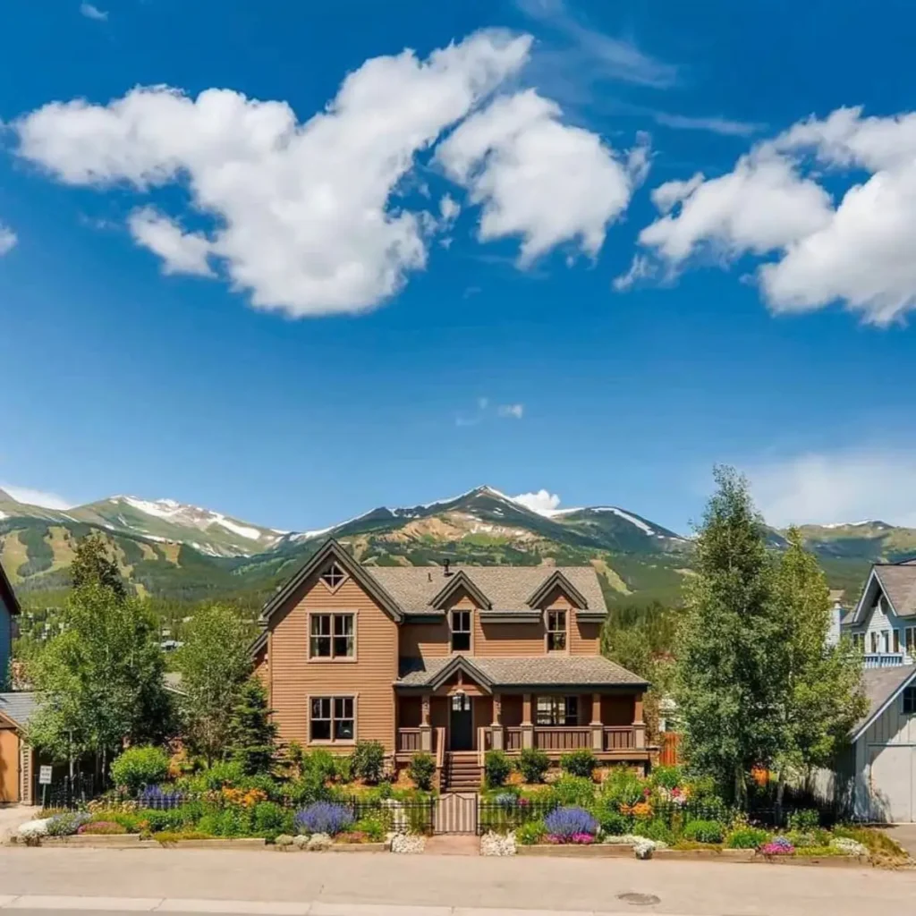 A luxury mountain home with a colorful perennial flower garden in front and snow-capped peaks behind.