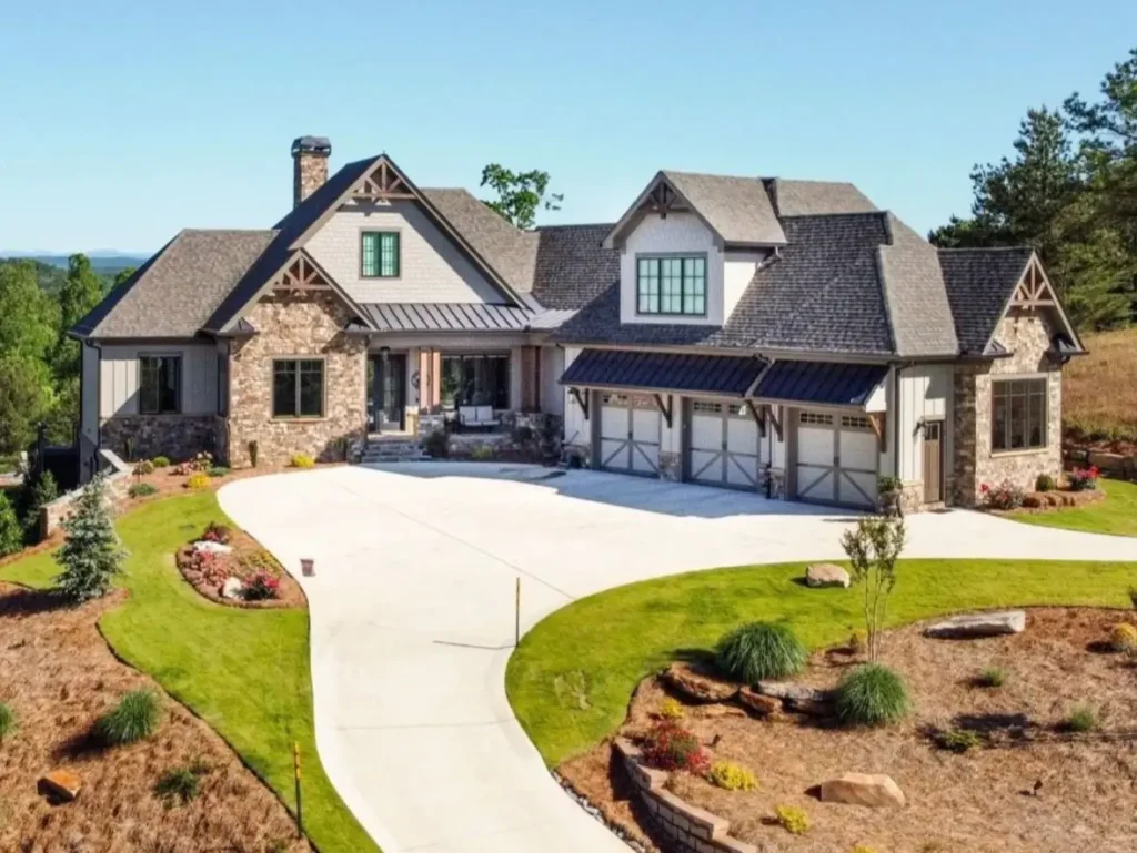 A luxury craftsman mountain home with a curving concrete driveway, stone accents, and a landscaped yard.
