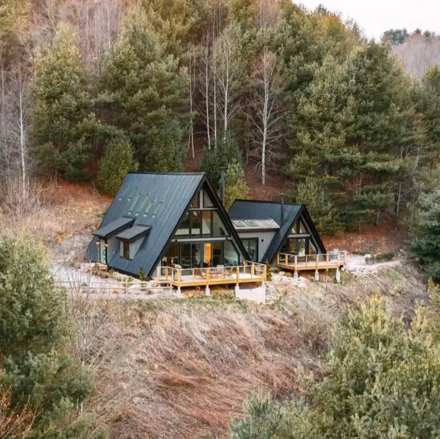Two modern black A-frame cabins with glass fronts and wooden decks built into a wooded hillside.