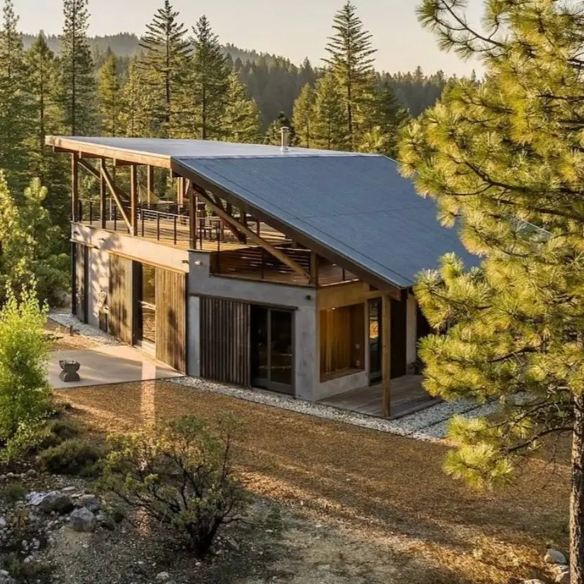 A modern mountain cabin with a large shed roof and wood accents set within a pine forest clearing.