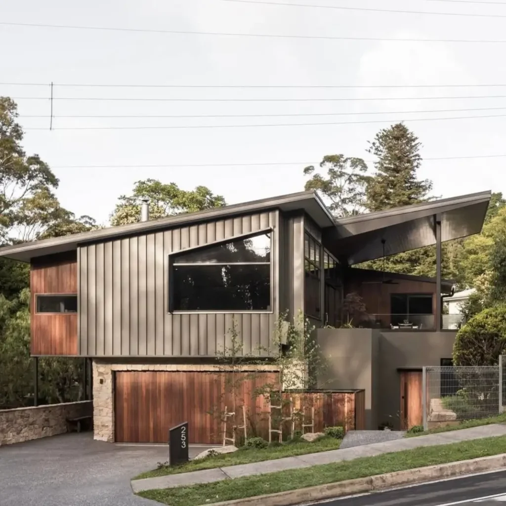 A mid-century modern inspired mountain home with an angled roof, metal siding, and a wooden garage door.