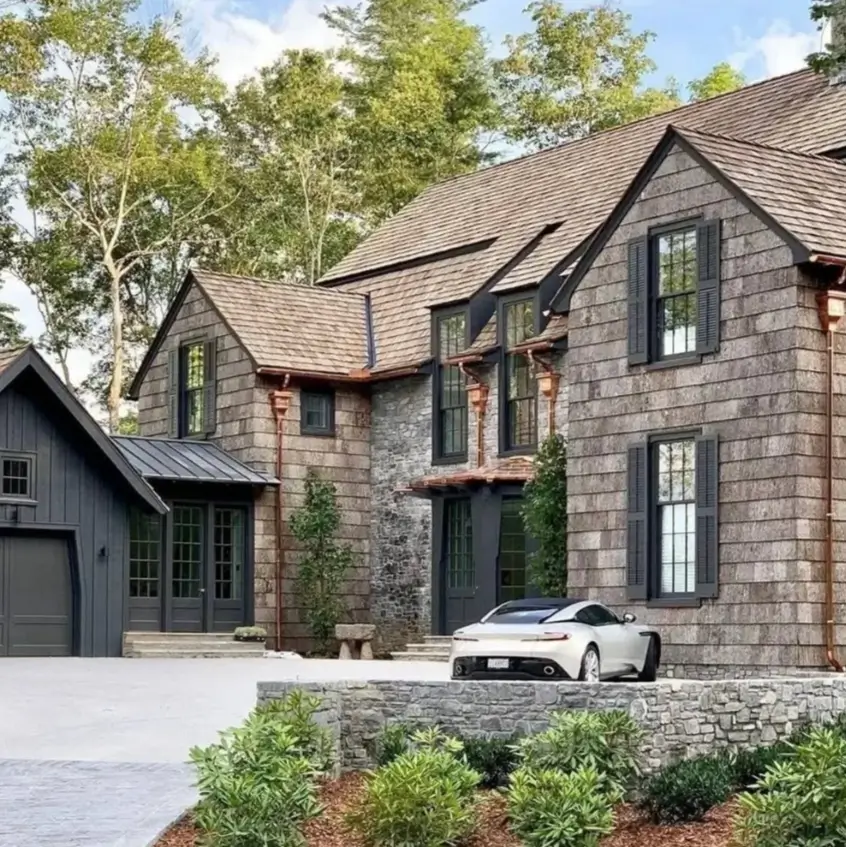 Exterior of a luxury mountain house with gray cedar shake siding, stone accents, and black shutters.