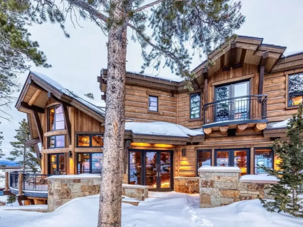Exterior of a grand log and stone mountain home covered in snow during winter.