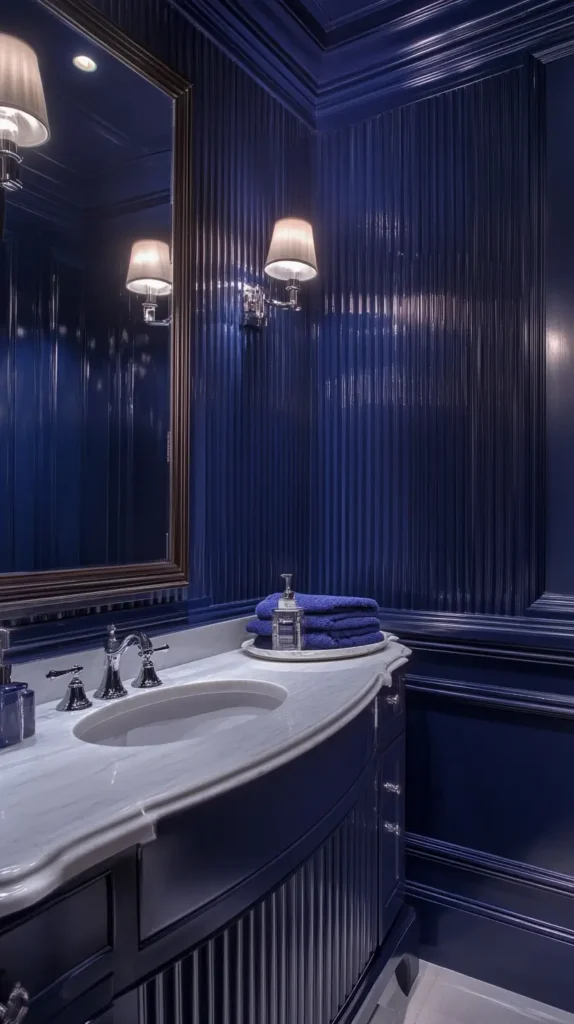 Elegant traditional bathroom featuring high-gloss navy blue vertically reeded paneling covering walls and the curved vanity base, contrasted by a white marble countertop and lit by traditional wall sconces.