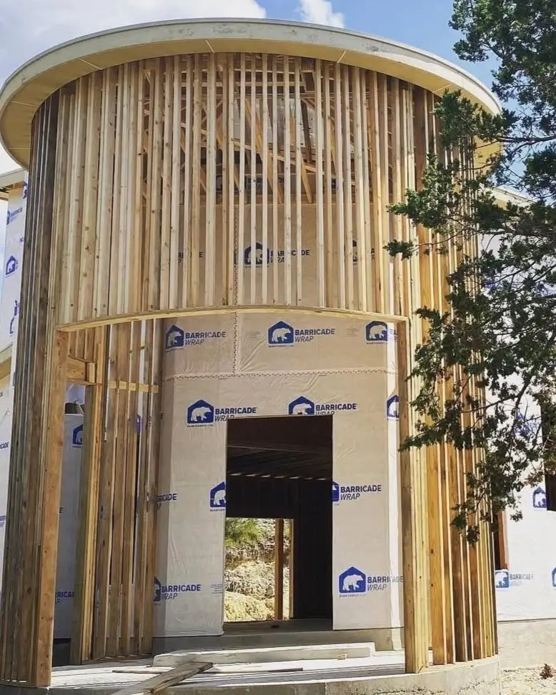 The wood-framed structure of a silo tower under construction, revealing the vertical studs that create the curve.