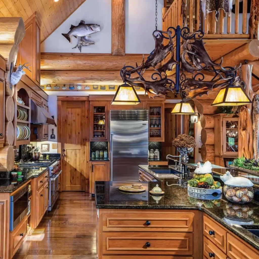 Modern log cabin kitchen with wood cabinetry, dark countertops, and antler chandelier.