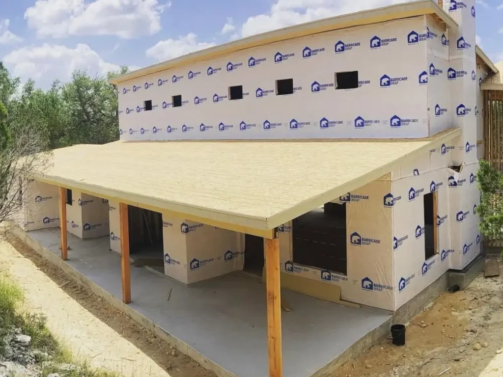 The connected rectangular portion of a modern farmhouse under construction, featuring a long covered porch.